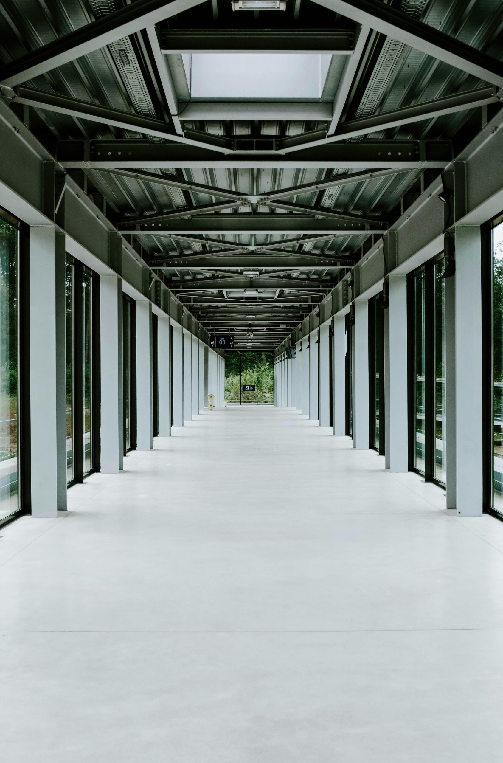 Empty modern glass corridor with metal framework and natural light entering through windows.